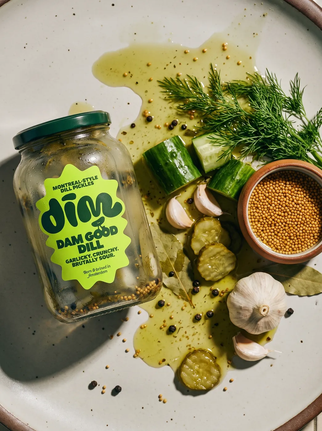 Dim Pickles jar on a plate with brine, dill, garlic and mustard seeds
