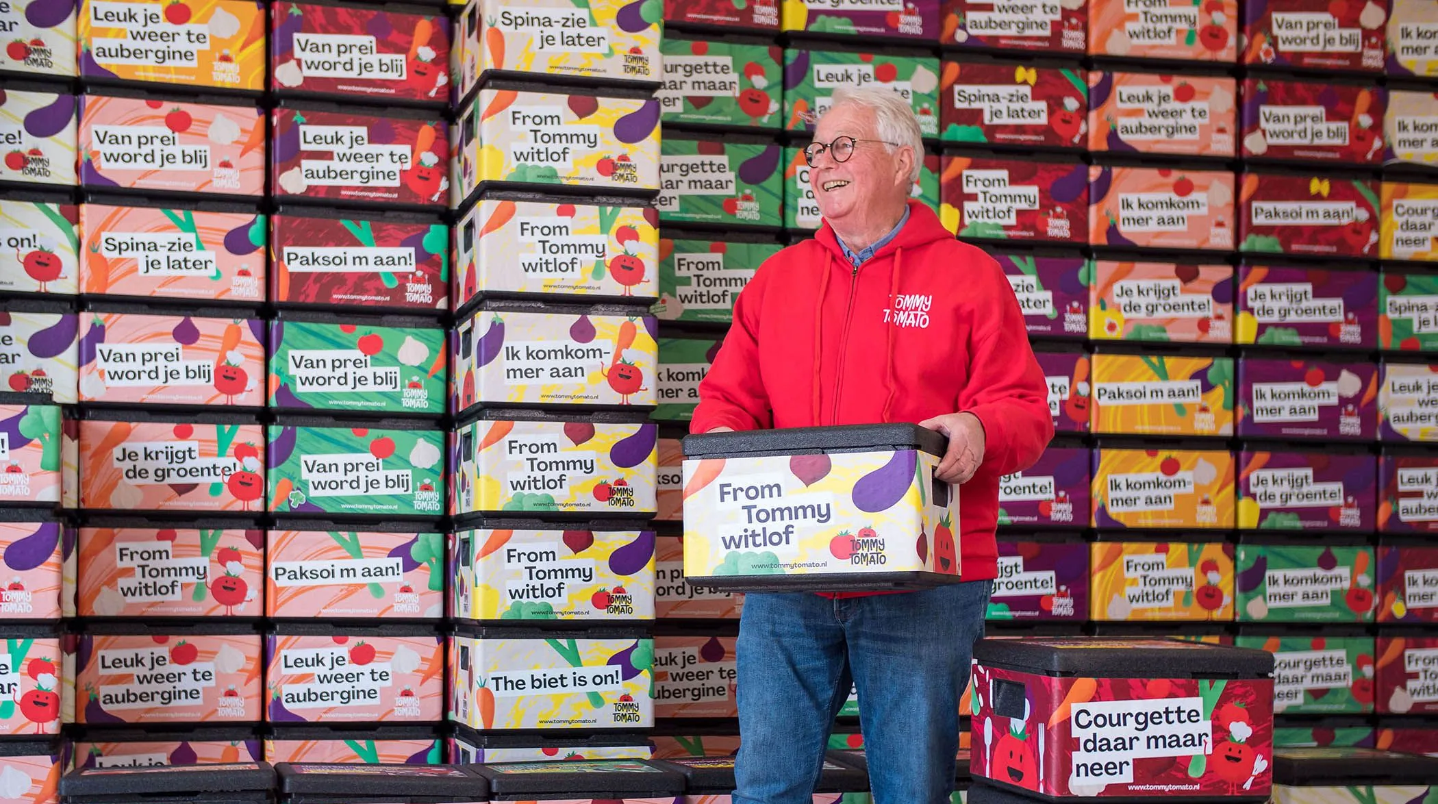 TommyTomato founder holding a lunch box in front of a wall of stacked boxes